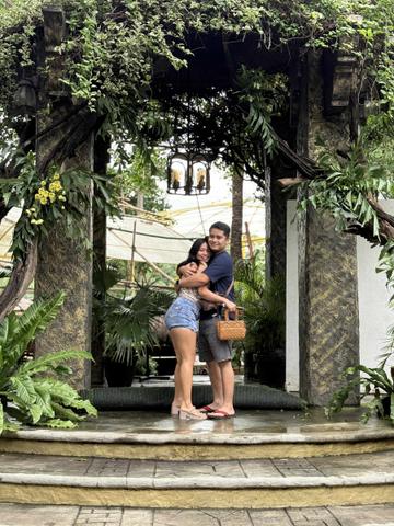 Rica Mae and Mark Lino embracing beneath a leafy stone arch in a garden